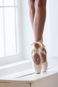 Women feet in pink pointe shoes with a bow are dancing on tiptoes